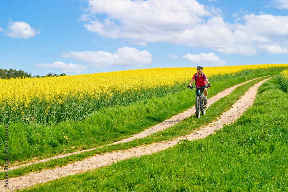 nice senior woman riding her electric mountainbike between blooming rape fields in spring near Stuttgart, Germany nice senior woman riding her electric mountainbike between blooming rape fields in spring near Stuttgart, Germany