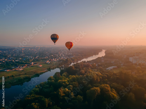 Two colorful air balloons flying over green park and river in small european city at summer sunrise