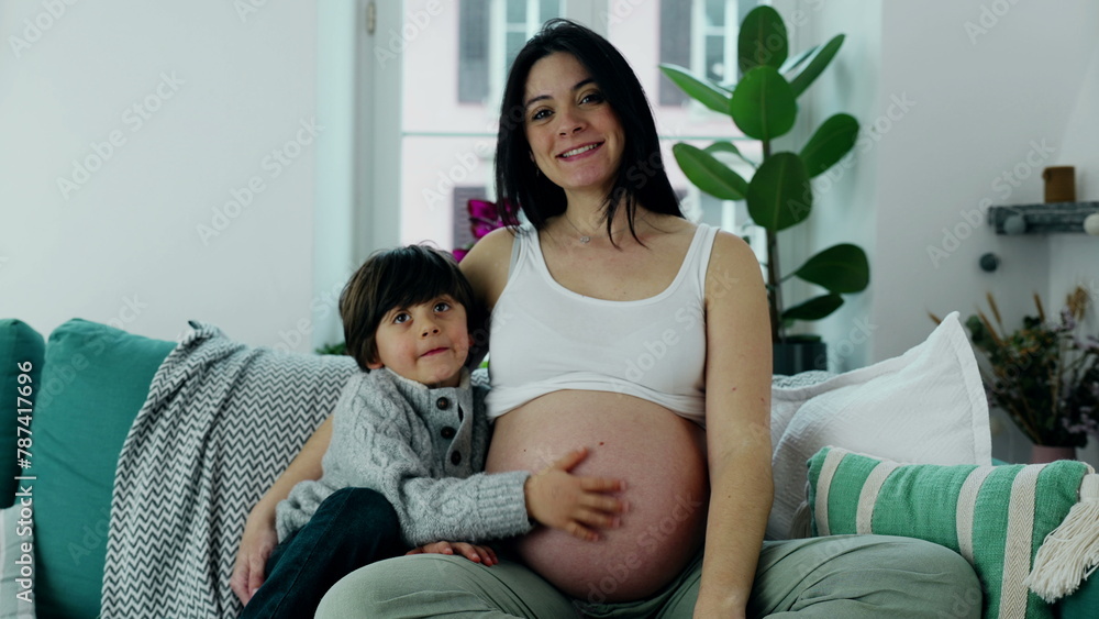 Joyful Family Scene with Young Boy and Pregnant Mother on Sofa, Smiling at Camera, 5-Year-Old Gently rubbing Mom's Belly, Capturing the Essence of Maternal Love Joyful Family Scene with Young Boy and Pregnant Mother on Sofa, Smiling at Camera, 5-Year-Old Gently rubbing Mom's Belly, Capturing the Essence of Maternal Love