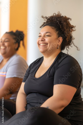 A cheerful, plus-sized woman enjoys a fitness session with a personal trainer, seated on an exercise mat with a smile