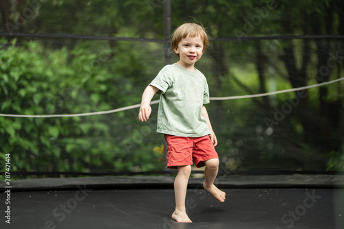 Cute little boy jumping on a trampoline in a backyard on warm and sunny summer day. Sports and exercises for children. Summer outdoor activities.