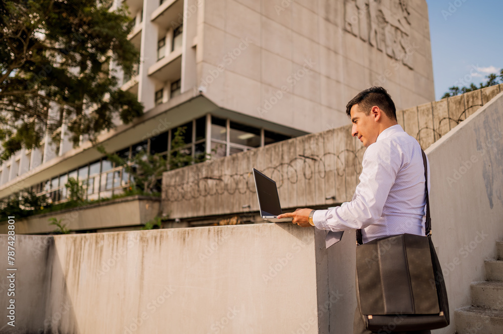 A young Latin man working on his laptop outdoors. The man blogging, chatting online, and checking email. Student learning online. A young Latin man working on his laptop outdoors. The man blogging, chatting online, and checking email. Student learning online.