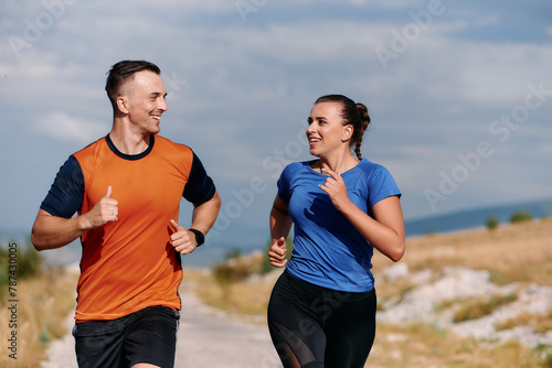 A couple dressed in sportswear runs along a scenic road during an early morning workout, enjoying the fresh air and maintaining a healthy lifestyle © .shock