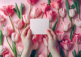 Creative floral concept. Pair of hand holding a blank card note surrounded with bed of seamless pink and red blooming tulips flowers leaf flora. Mock up presentation. top view, flat lay