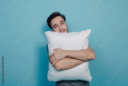 Young man with soft pillow on blue background sleeping like baby, enjoying sweet dreams, feeling relaxed, over blue wall