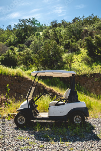 Leisure day on the course: white golf cart parked against a lush green hill under the bright sunny sky