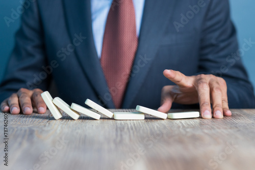 Business man stoping domino effect by his hand, business strategy background image, wearing blue suit and red tie