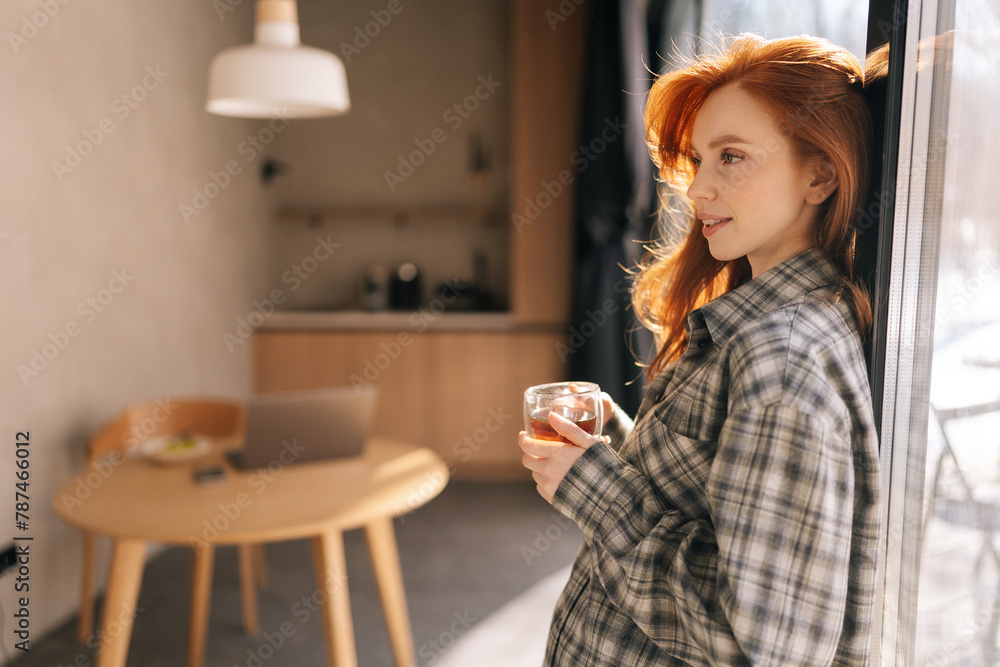 Side view portrait of pretty young woman holding cup enjoy smell coffee or tea and drinking with happiness standing by window on sunny morning. Smiling female enjoys good morning feels stress free.