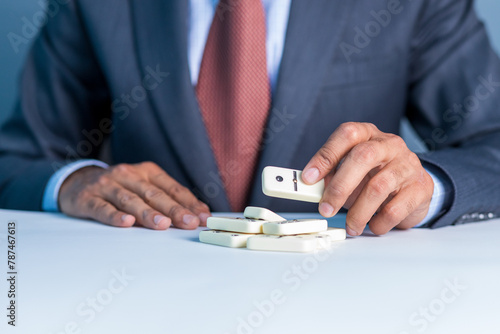 Business man stoping domino effect by his hand, business strategy background image, wearing blue suit and red tie photo