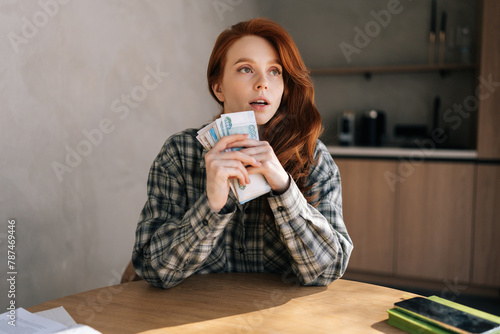 Vertical shot of unhappy young woman holding banknotes feeling stress about unemployment at home workplace. Upset female holding money and disappointed about bad earnings salary.