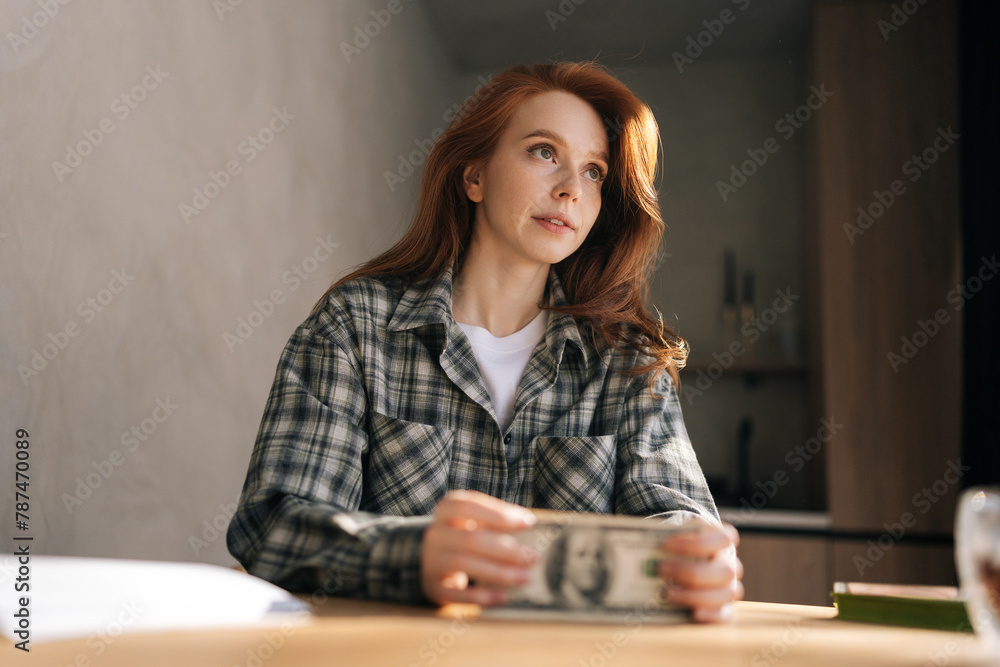 Low-angle view of thoughtful young woman holding banknotes feeling stress about unemployment at home workplace. Upset female holding money and disappointed about bad earnings salary. Low-angle view of thoughtful young woman holding banknotes feeling stress about unemployment at home workplace. Upset female holding money and disappointed about bad earnings salary.