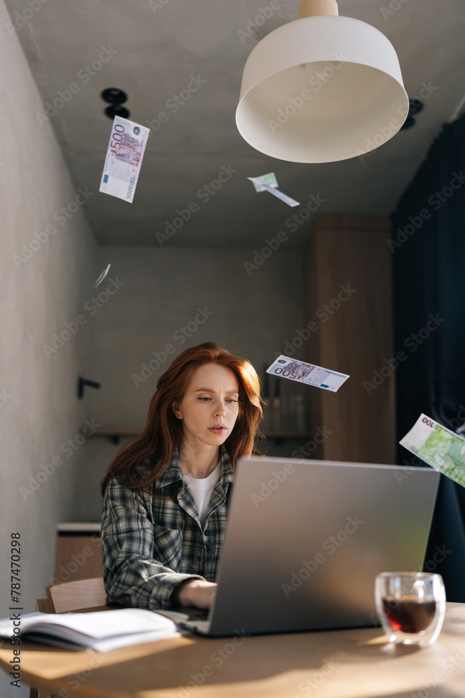 Vertical shot of money cash dollar rain falling on pretty young businesswoman sitting at home desk celebrating success, winning, goal achievement, good news, lottery jackpot luck. Career grow. Vertical shot of money cash dollar rain falling on pretty young businesswoman sitting at home desk celebrating success, winning, goal achievement, good news, lottery jackpot luck. Career grow.