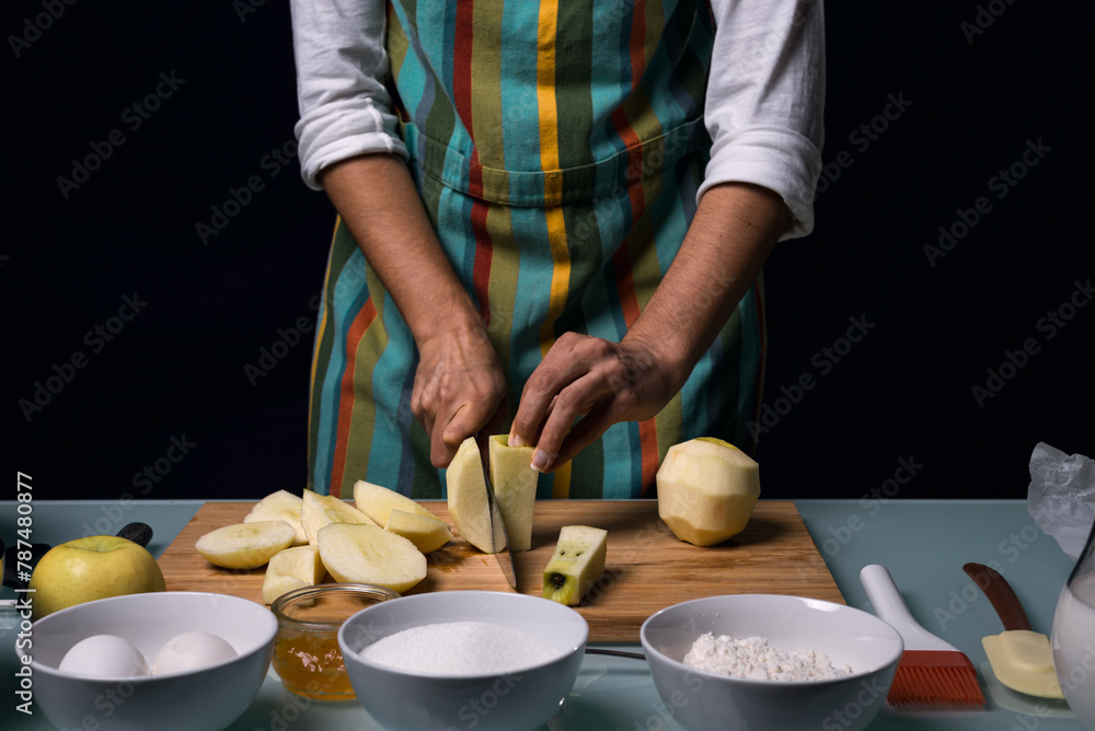 Working in the kitchen. Half-length photography. Detail of hands cutting apple into pieces. Black background. Working in the kitchen. Half-length photography. Detail of hands cutting apple into pieces. Black background.