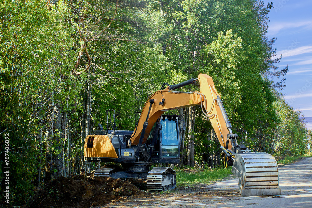 Excavator works in forest belt near country road. Excavator works in forest belt near country road.