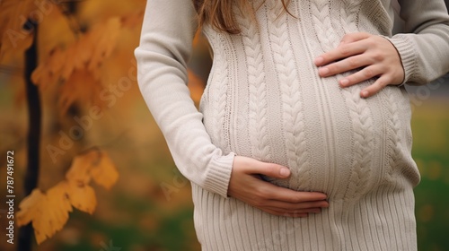 Close up of pregnant woman in sweater touching her belly in the autumn park