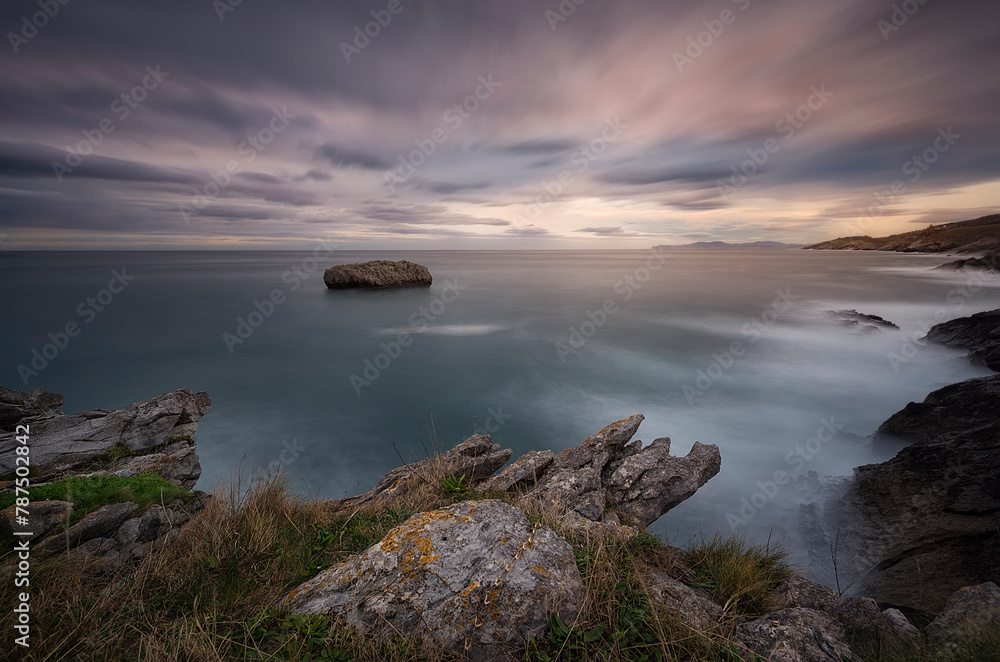Sunset in Cotonera cove in Islares, Cantabria with a cloudy sky and warm colors and the rock formations in the foreground