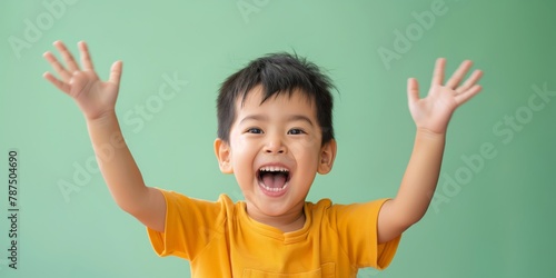 Southeast Asian boy laughing heartily, clad in a white shirt against a light mint green background, capturing the essence of joyful childhood.