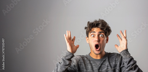 A man with a shocked expression on his face. He is wearing a gray sweater and has his hands raised in the air. a french young man looking surprised with one of his hands raised photo