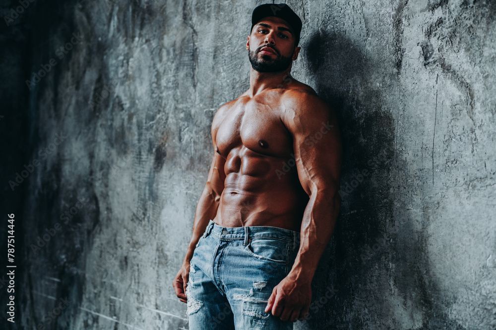 Obraz premium Young strong man bodybuilder in cap on stone wall background