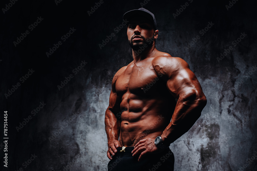 Obraz premium Young strong man bodybuilder in cap on stone wall background