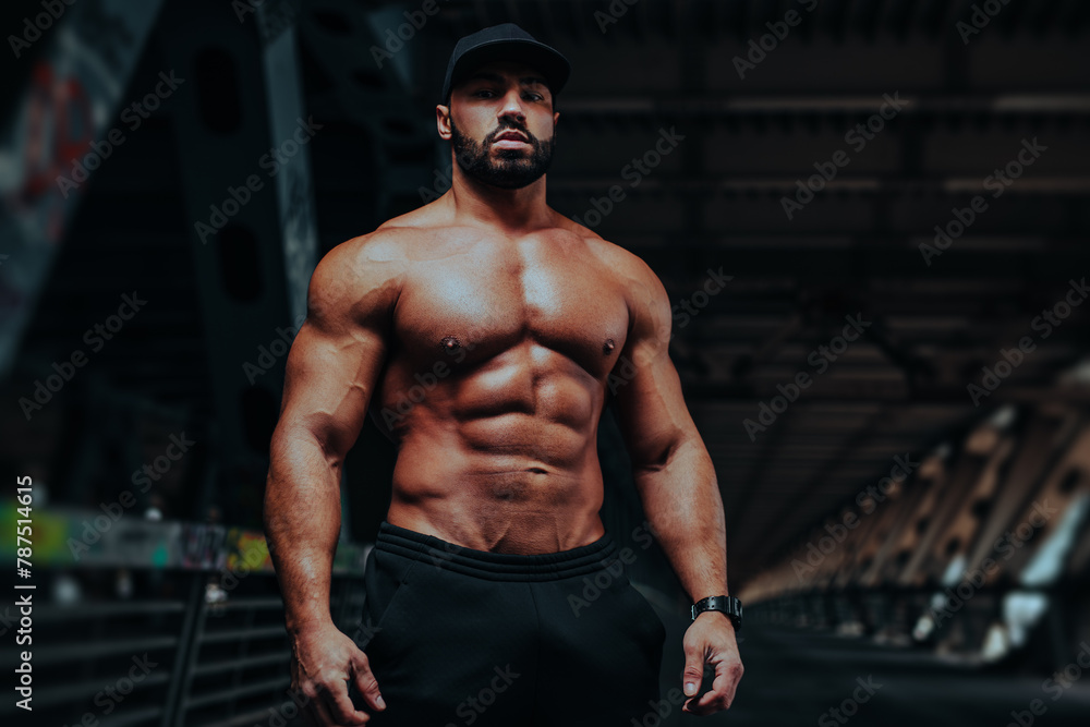 Naklejka premium Young strong man bodybuilder posing on urban background