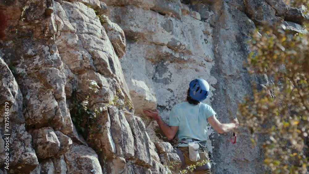 A rock climber in motion, deliberately navigating a challenging limestone cliff, is the focal point of this cinematic ProRes capture. The climber's blue helmet is discernible as they assess their next A rock climber in motion, deliberately navigating a challenging limestone cliff, is the focal point of this cinematic ProRes capture. The climber's blue helmet is discernible as they assess their next