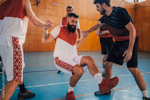 Quadro em tela Diverse men helping their teammate to get up after falling down after a foul