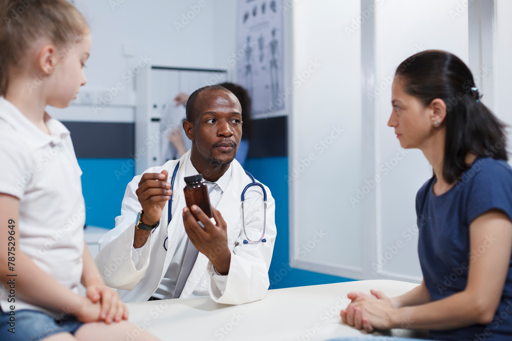 Obraz premium Caucasian mother and daughter intently listening to an African American physician describing the bottle of medicine. They discuss health care with an emphasis on thorough evaluation and treatment.