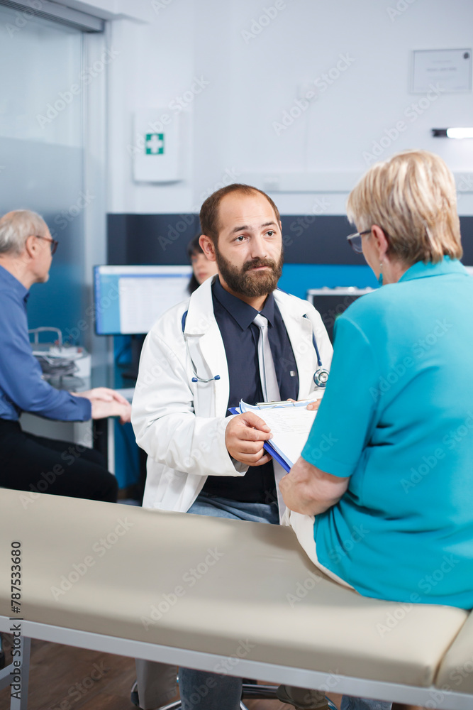 Obraz premium Elderly woman fills out medical forms and talks with doctor about her treatment. Portrait of male practitioner asking senior patient to sign documents for physiotherapy treatment.