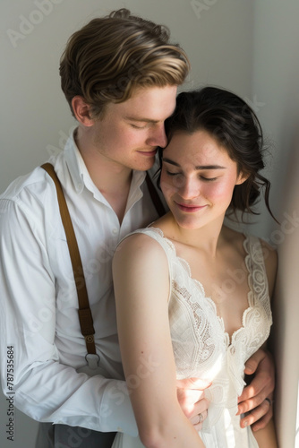 A young man and woman, dressed in vintage-inspired attire, share a close moment by a window bathed in gentle light