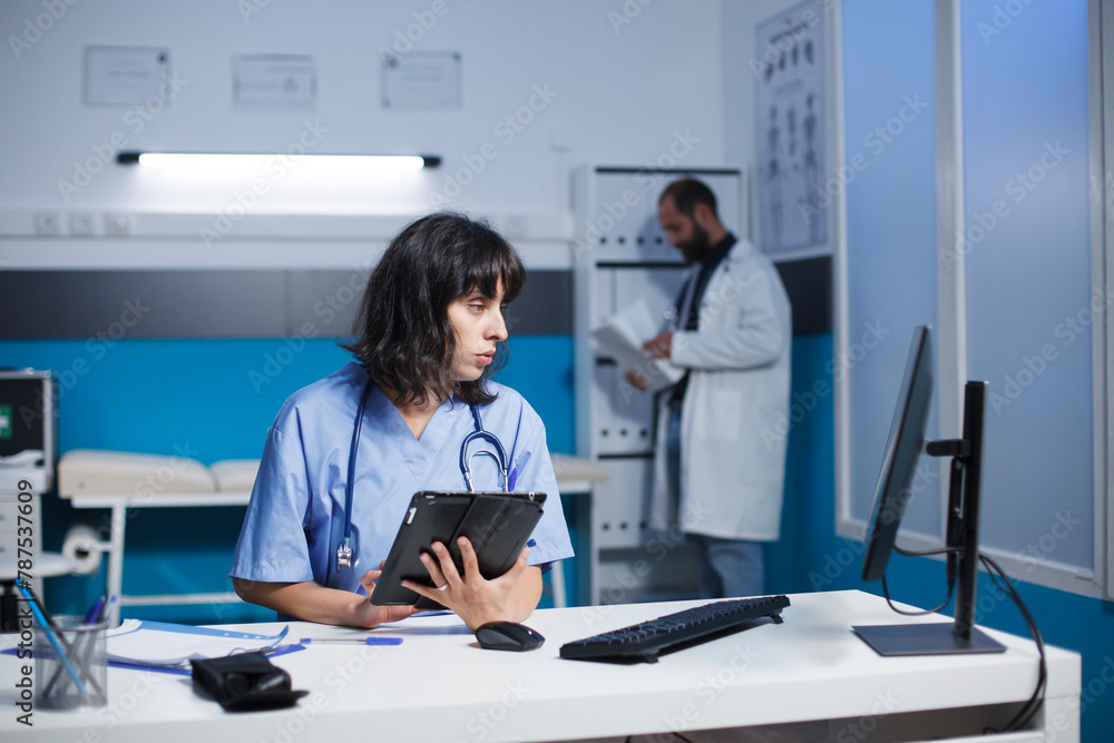 Female nurse uses a smart tablet and computer for medical information and checkups. While examining patient data on desktop pc, healthcare professional holds a gadget with a touch screen. Female nurse uses a smart tablet and computer for medical information and checkups. While examining patient data on desktop pc, healthcare professional holds a gadget with a touch screen.