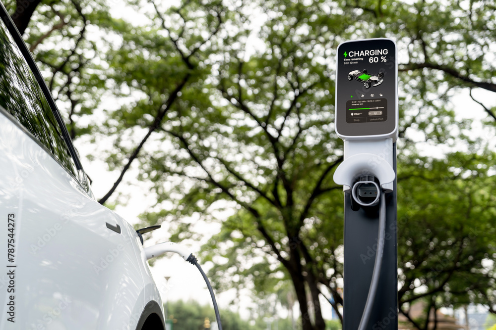 Obraz premium EV electric vehicle recharging battery from EV charging station in national park or outdoor forest scenic. Natural protection with eco friendly EV car travel in the summer woods. Exalt