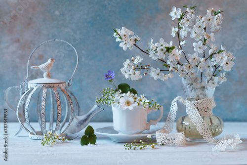 Spring floral still life. Blooming cherry plum branches in a vase, a cup and a teapot on a white wooden table.
