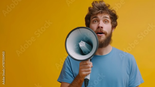 Young bearded man in blue shirt holding megaphone on yellow background