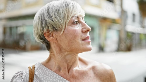 Elegant senior hispanic woman with short grey hair gazing upward on a busy urban street. photo