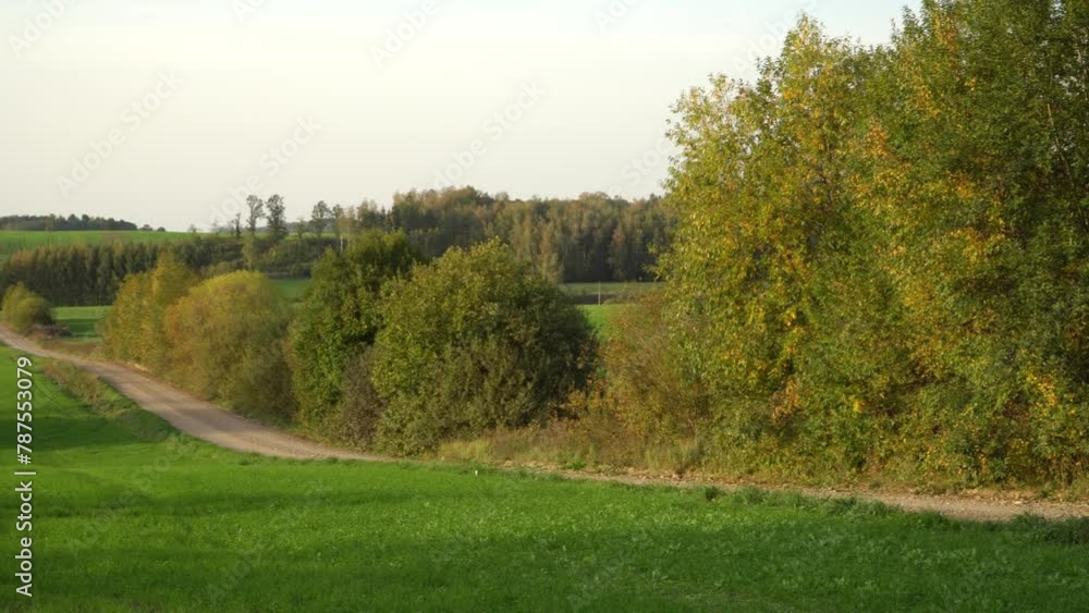 Idyllic countryside landscape in the afternoon with a lonely gravel road winding over the hills in early autumn. Scenic panorama in a rural environment with farmland and straw bale rolls on a field. Idyllic countryside landscape in the afternoon with a lonely gravel road winding over the hills in early autumn. Scenic panorama in a rural environment with farmland and straw bale rolls on a field.