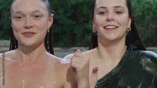 Two women emerge from a pool and smile at each other