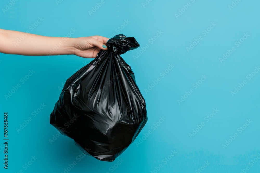Go Green for Earth Day: Hand Holding Black Garbage Bag on Blue Background, reduce, reuse, recycle Go Green for Earth Day: Hand Holding Black Garbage Bag on Blue Background, reduce, reuse, recycle