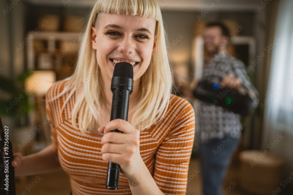 Adult woman sing karaoke on microphone with man in the background Adult woman sing karaoke on microphone with man in the background