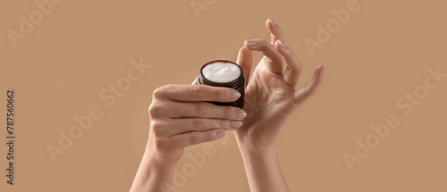 Hands holding cosmetic cream on beige background