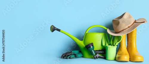 Composition with watering can, rubber boots and hat on blue background. Garden tools photo