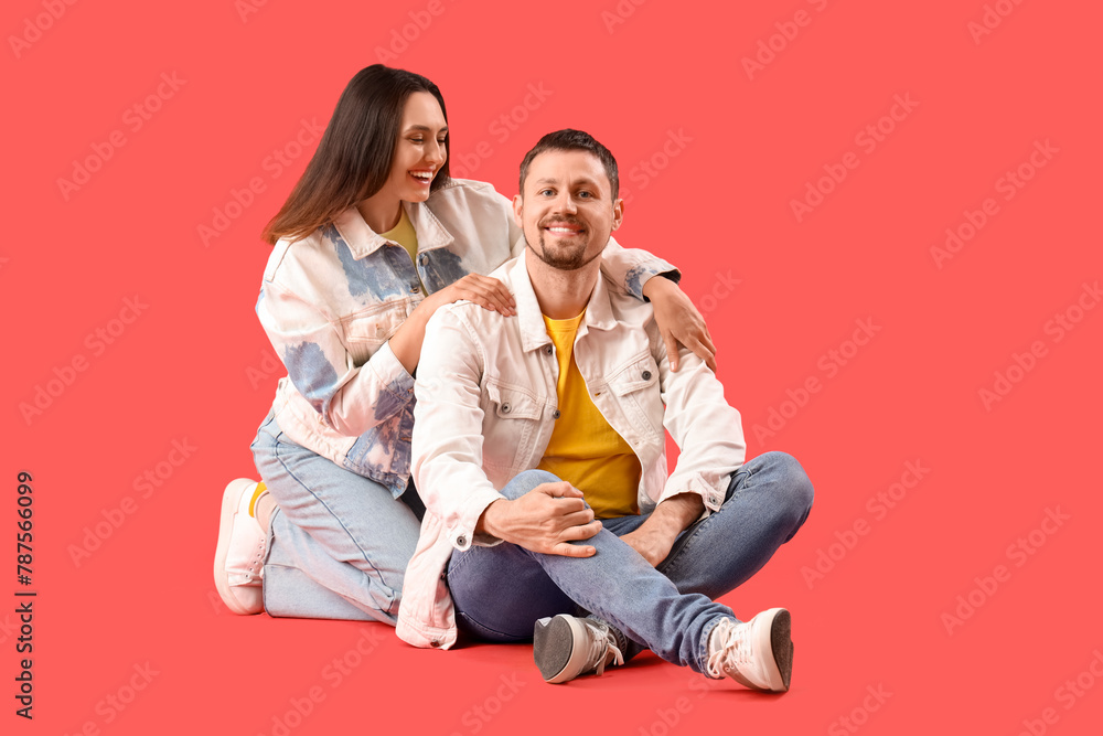 Happy young couple sitting on red background Happy young couple sitting on red background