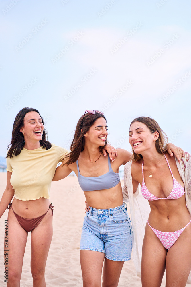 Vertical pic of Three young Caucasian beautiful women friends embracing in swimwear posing cheerful on beach holidays. Group of gen z female hugging standing smiling on sunny summer time Vertical pic of Three young Caucasian beautiful women friends embracing in swimwear posing cheerful on beach holidays. Group of gen z female hugging standing smiling on sunny summer time