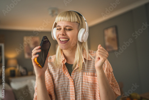 Young woman with headphones listen music and sign on mobile phone happy © Miljan Živković