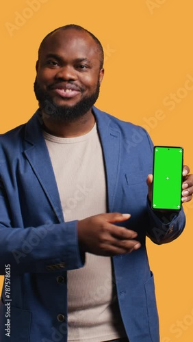 Vertical video Happy african american man holding green screen phone, doing recommendation. Cheerful BIPOC person presenting mockup device, giving thumbs up sign, studio background, camera B