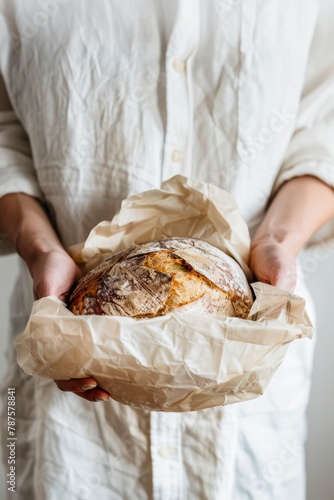 Freshly baked artisanal bread wrapped in parchment paper held by a person.