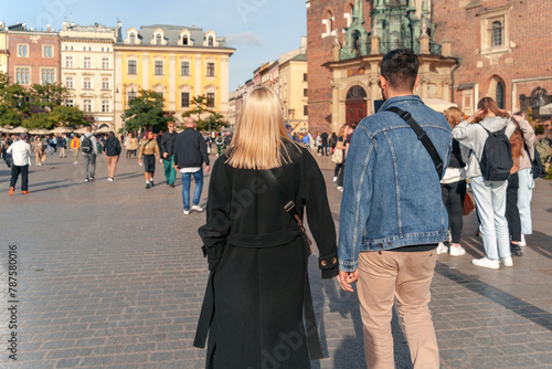 A Gen Z couple strolls through a vibrant city square surrounded by historic architecture under a clear blue sky, epitomizing urban exploration and cultural immersion
