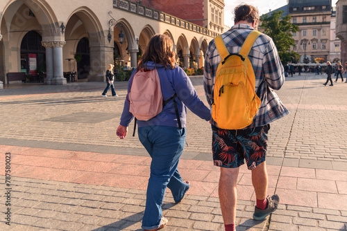 A couple of tourists with backpacks walk through the busy town square of the old town on a sunny day, reflecting the trends of urban travel and socializing among historical architecture