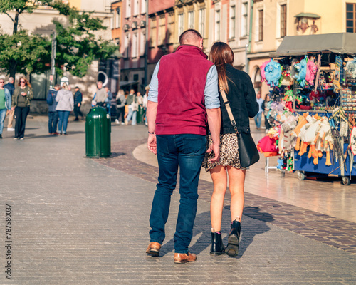 Urban Gen Z romance unfolds on a busy market street on a sunny afternoon, where a couple's stroll hand-in-hand becomes a symbol of love and connection in the heart of the city