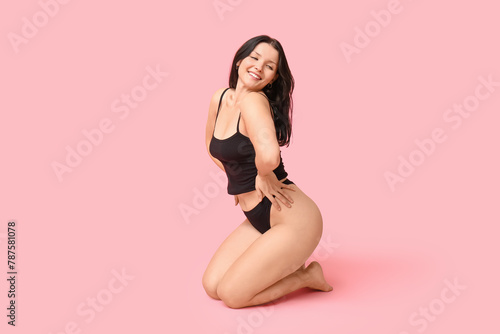 Body positive young woman in underwear sitting on pink background
